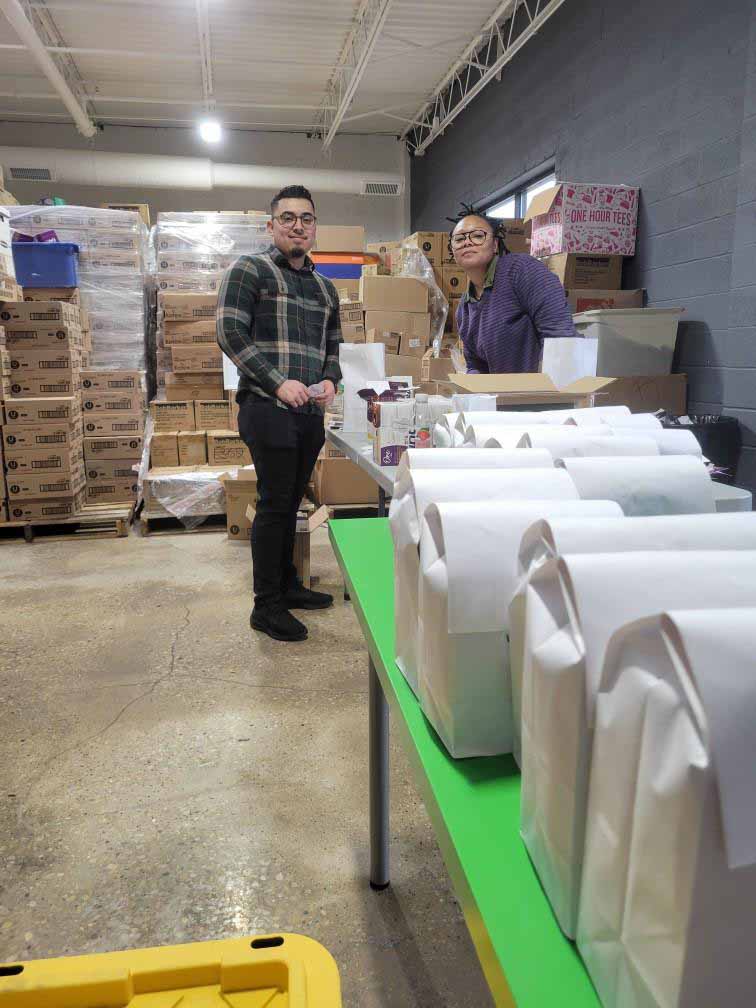 man and woman standing at table full of packed white bags