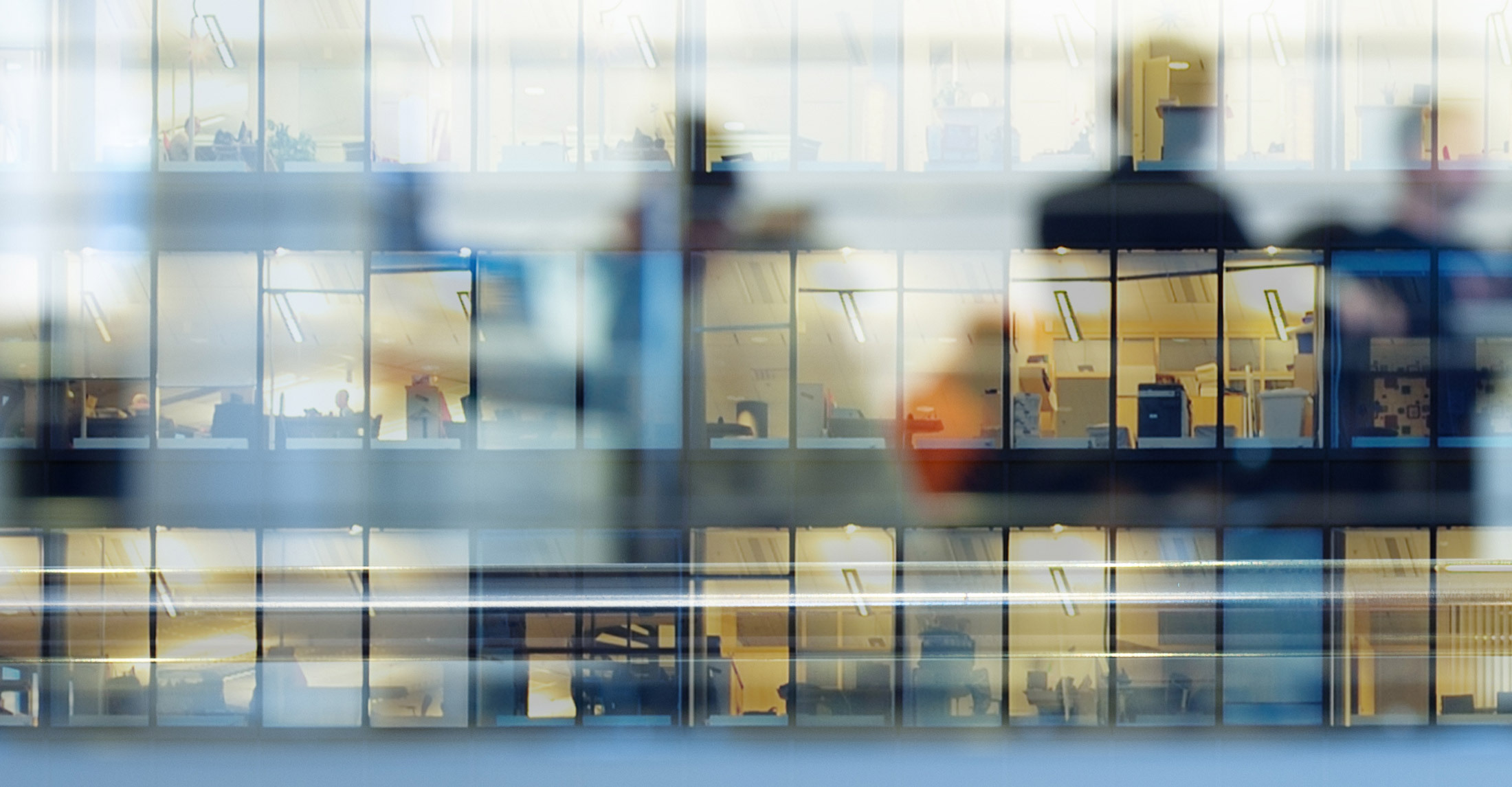 outside façade of glass windows of a multi-story building looking in multiple offices.