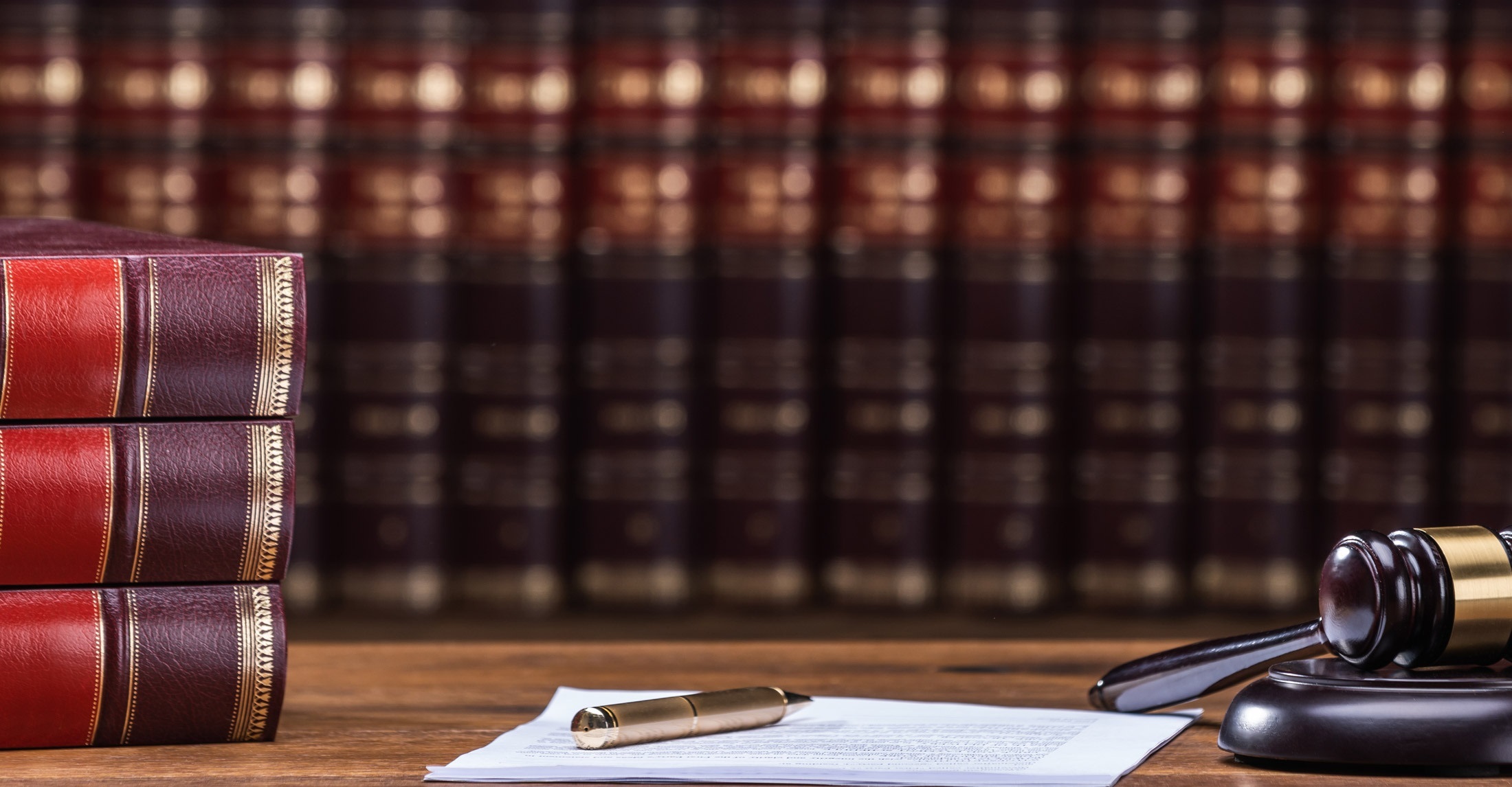 stack of 3 books in left foreground, gavel in right foreground, and books on shelf in background