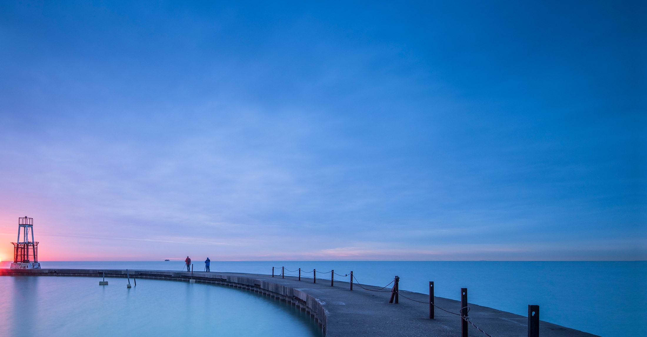 a lakeview with a walking path over the water with a blue and pink sunset