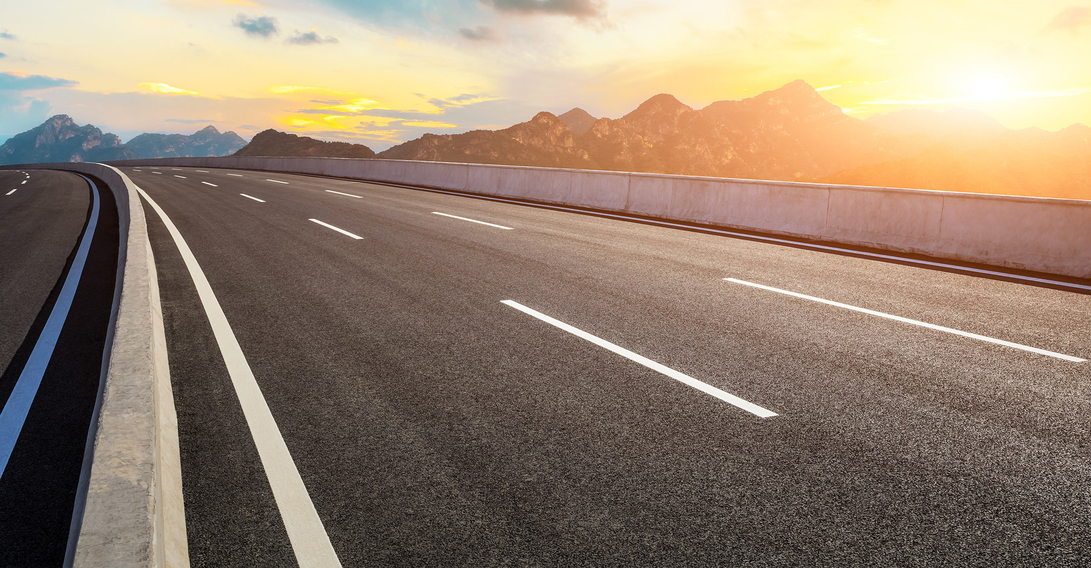 multi-lane highway in foreground with golden sunshine on mountains in background on right