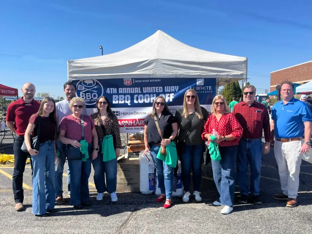 women and men standing in front of a large tent with a banner behind them for United Way